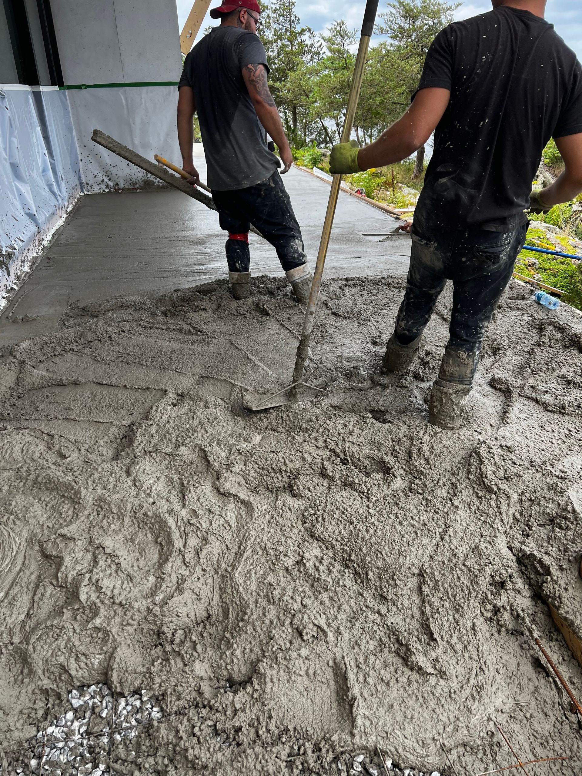 Two men are working on a concrete floor with shovels.