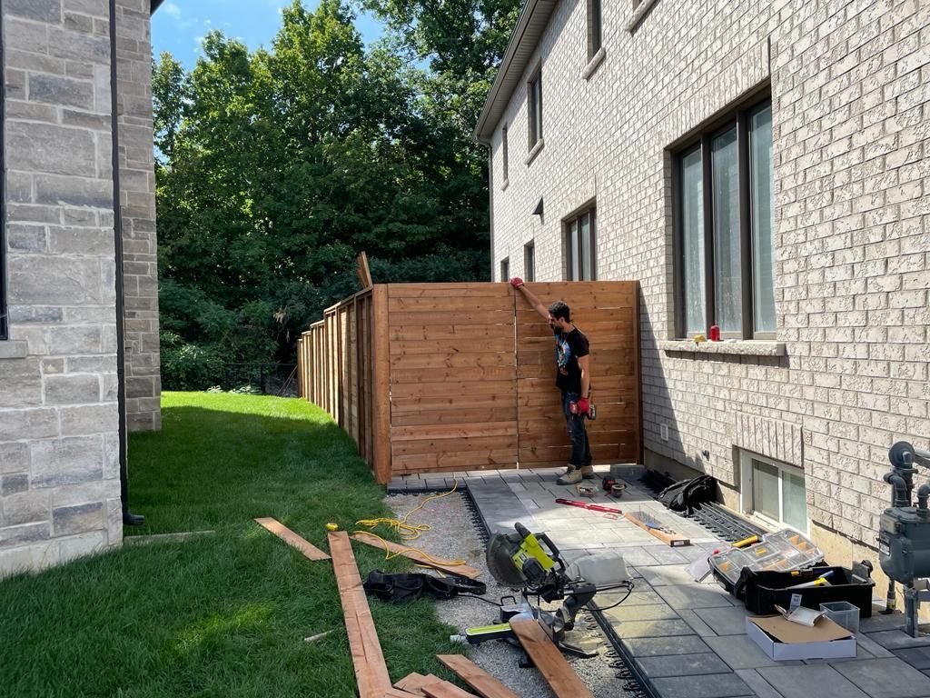 A man is building a wooden fence in the backyard of a house.