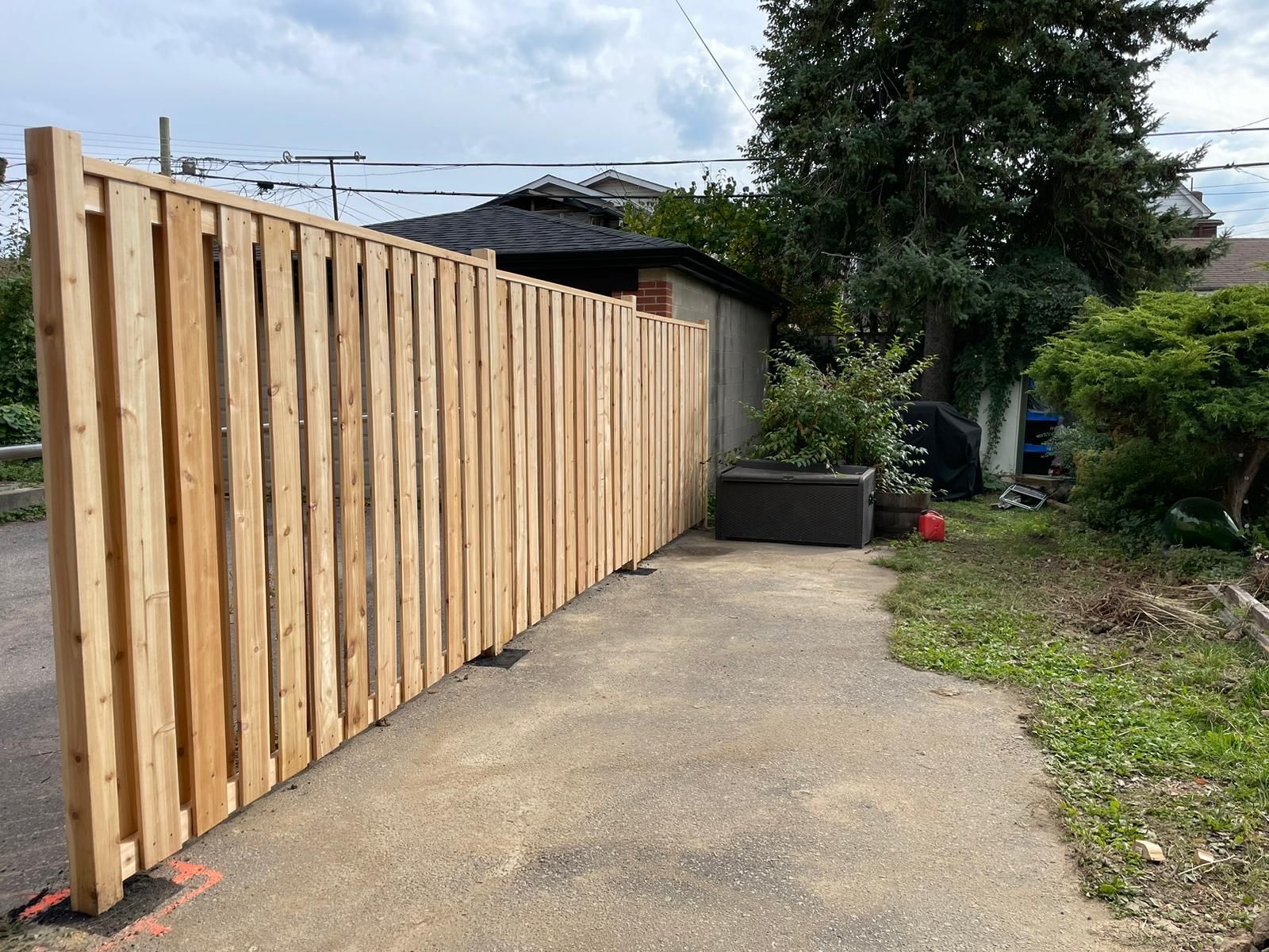 A wooden fence is sitting on the side of a road next to a house.