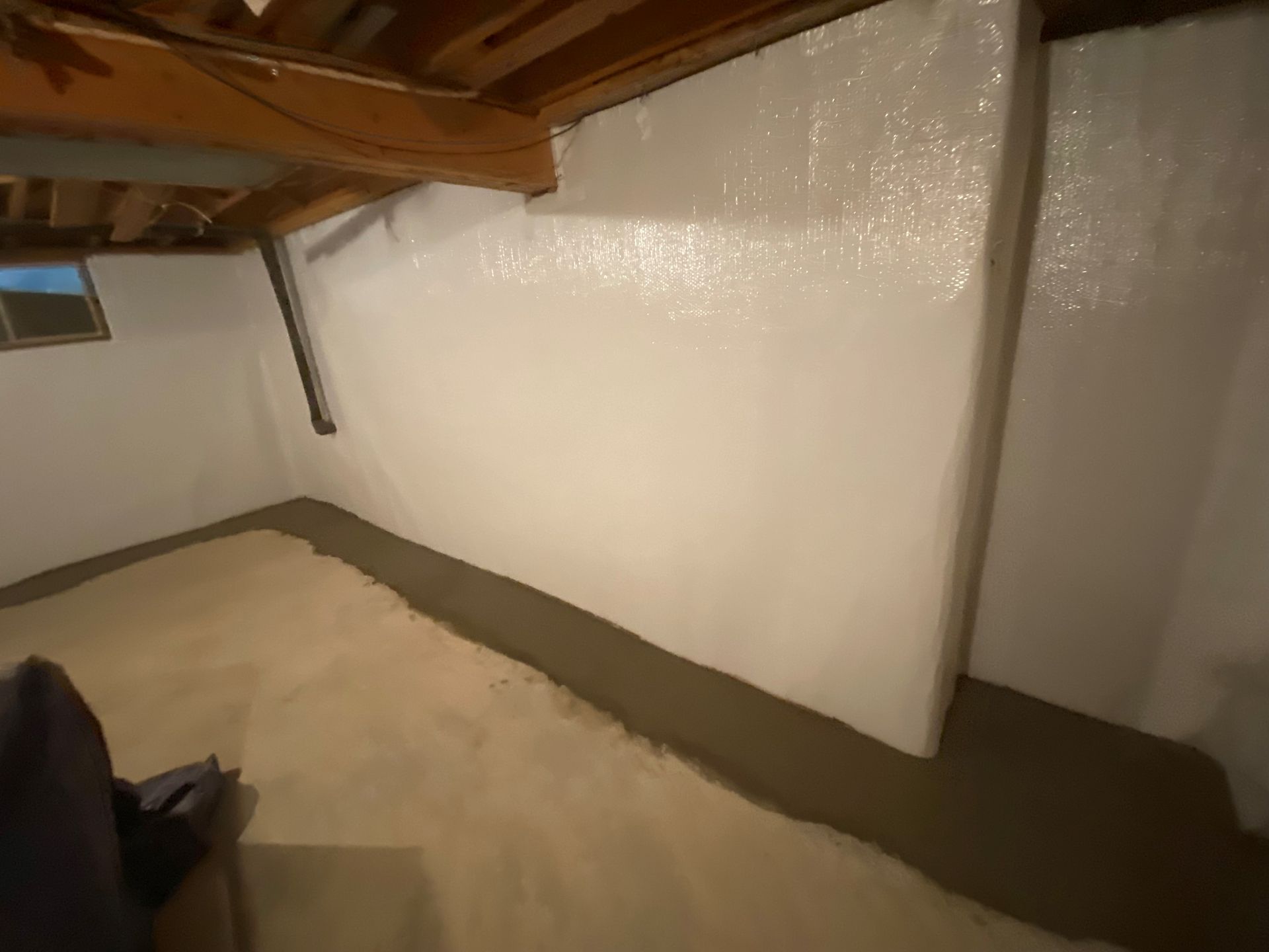 A basement with a white wall and a concrete floor.