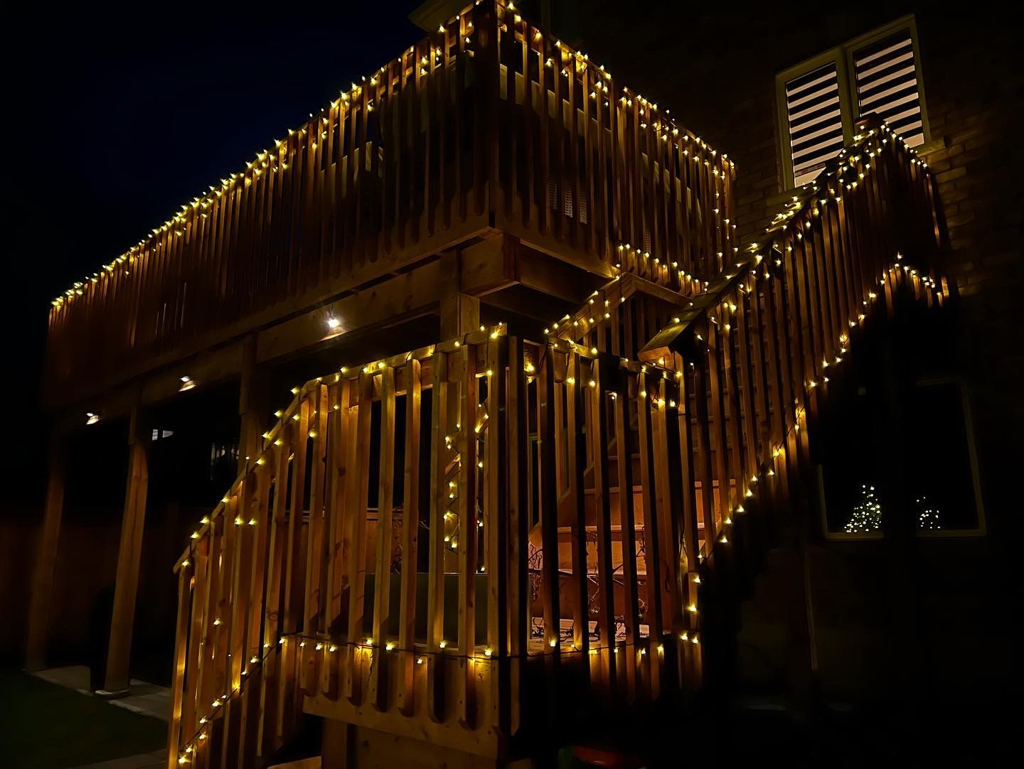 A wooden deck decorated with christmas lights at night.