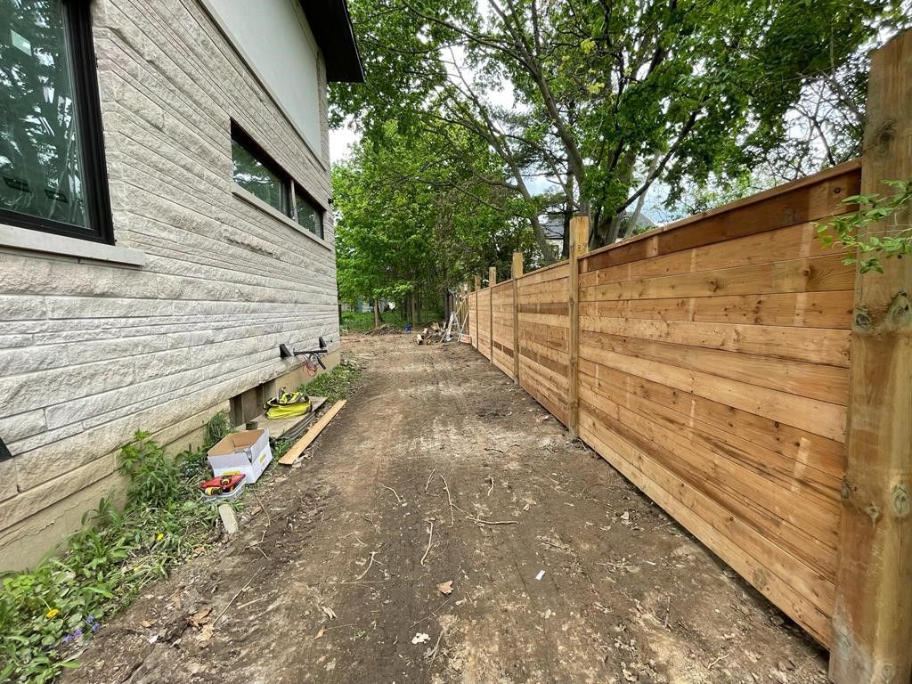 A wooden fence is being built in front of a brick house.