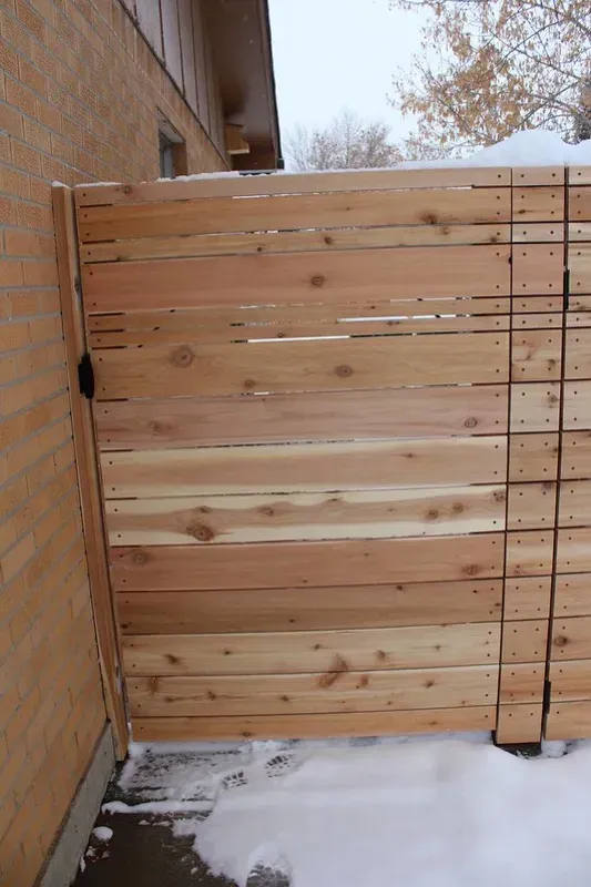 A wooden gate is sitting in the snow next to a brick building.