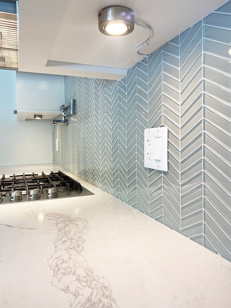 A kitchen with a stove , counter top , and chevron tiles on the wall.