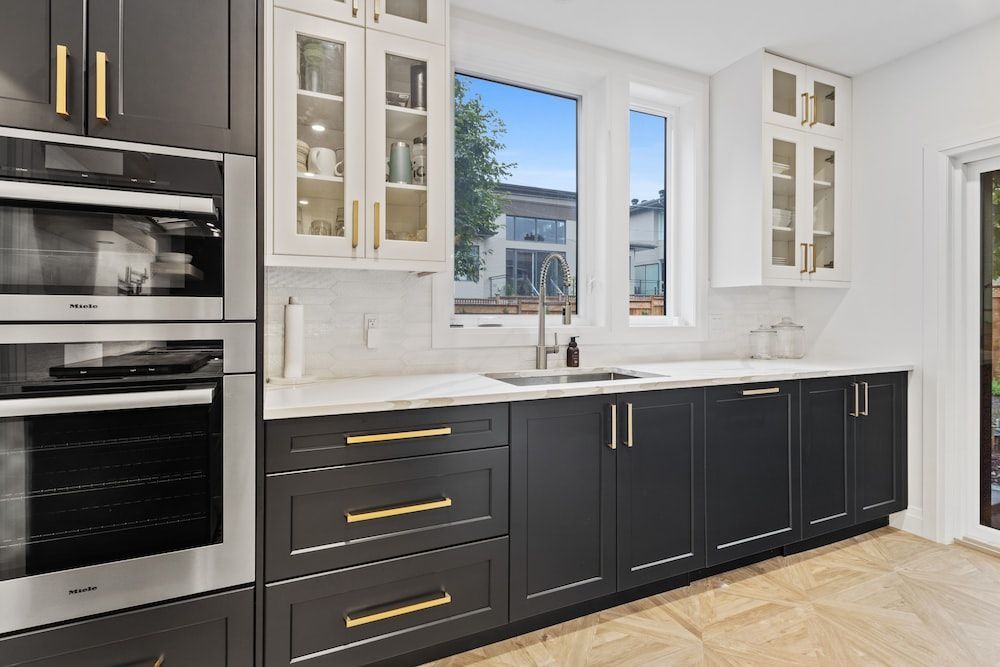 A kitchen with black cabinets , white counter tops , and stainless steel appliances.