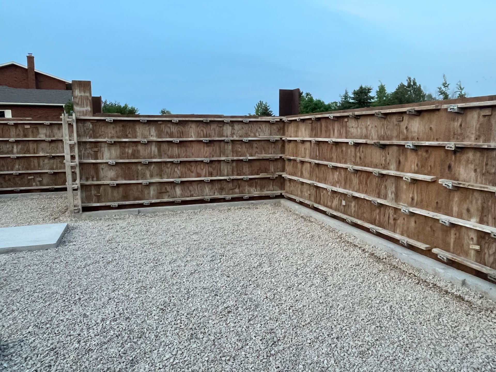 A wooden fence is surrounded by gravel and a house in the background.