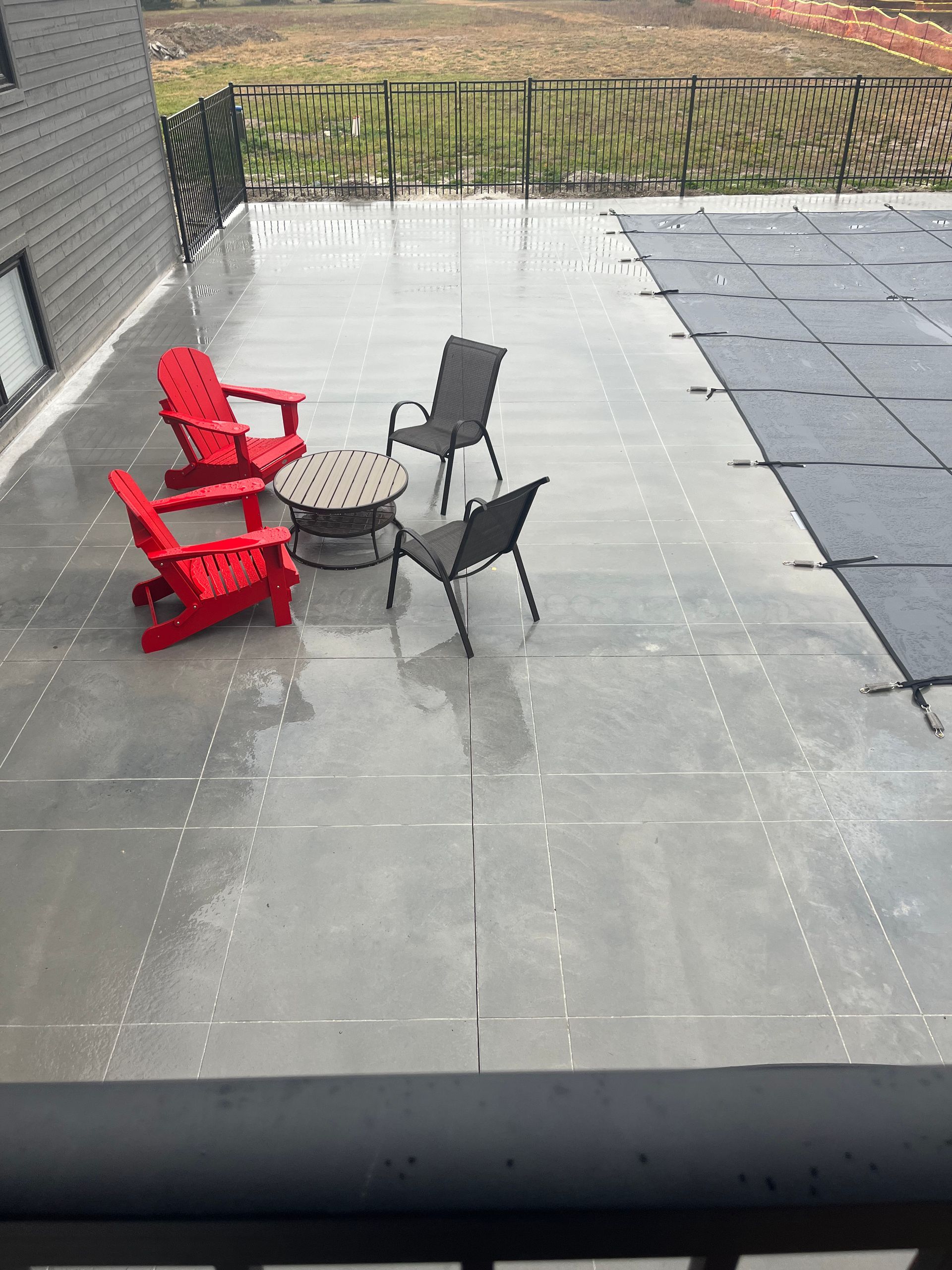 A patio with chairs , a table and a fire pit next to a pool.