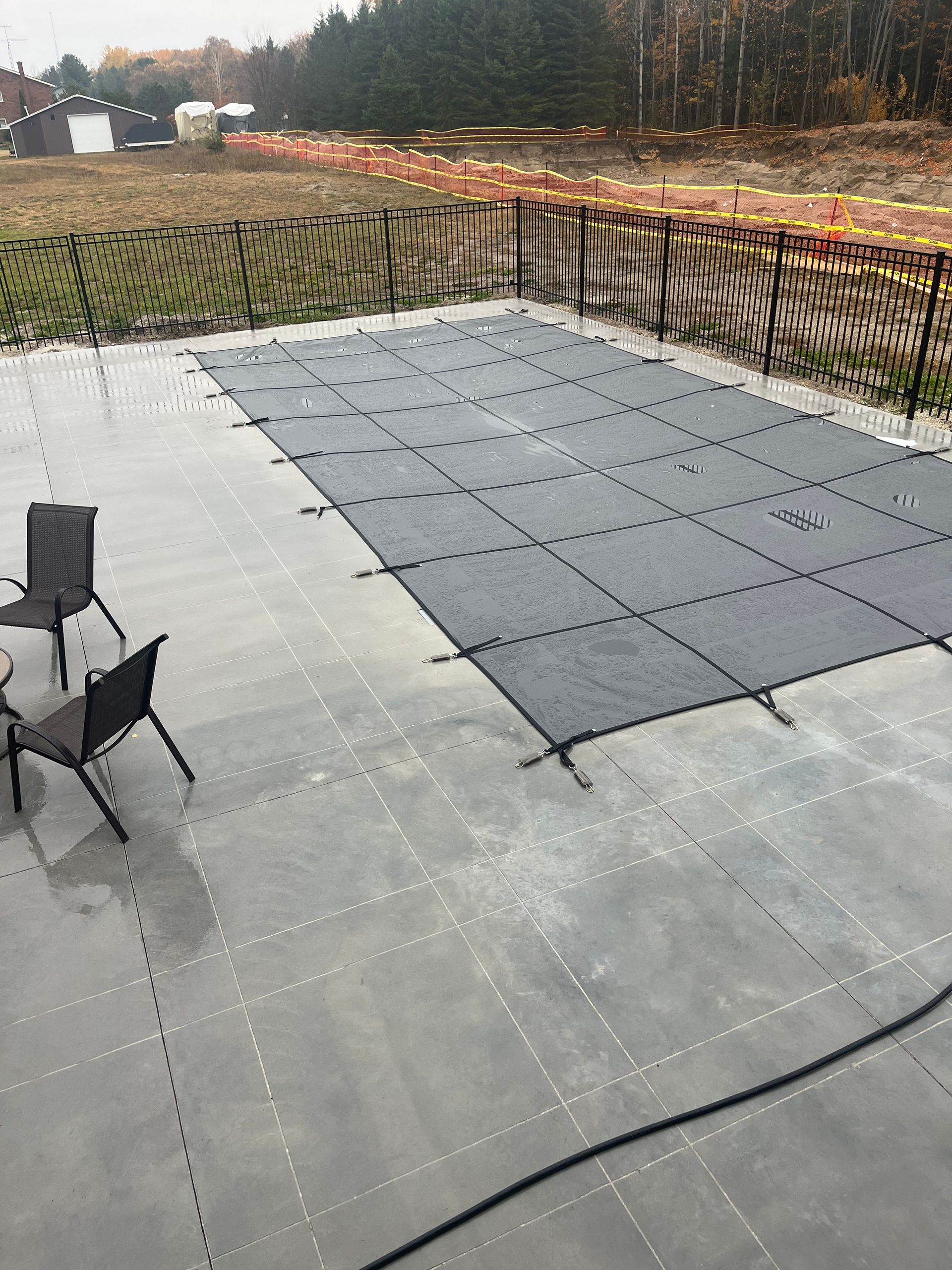 A swimming pool with a cover on it and chairs on a patio.