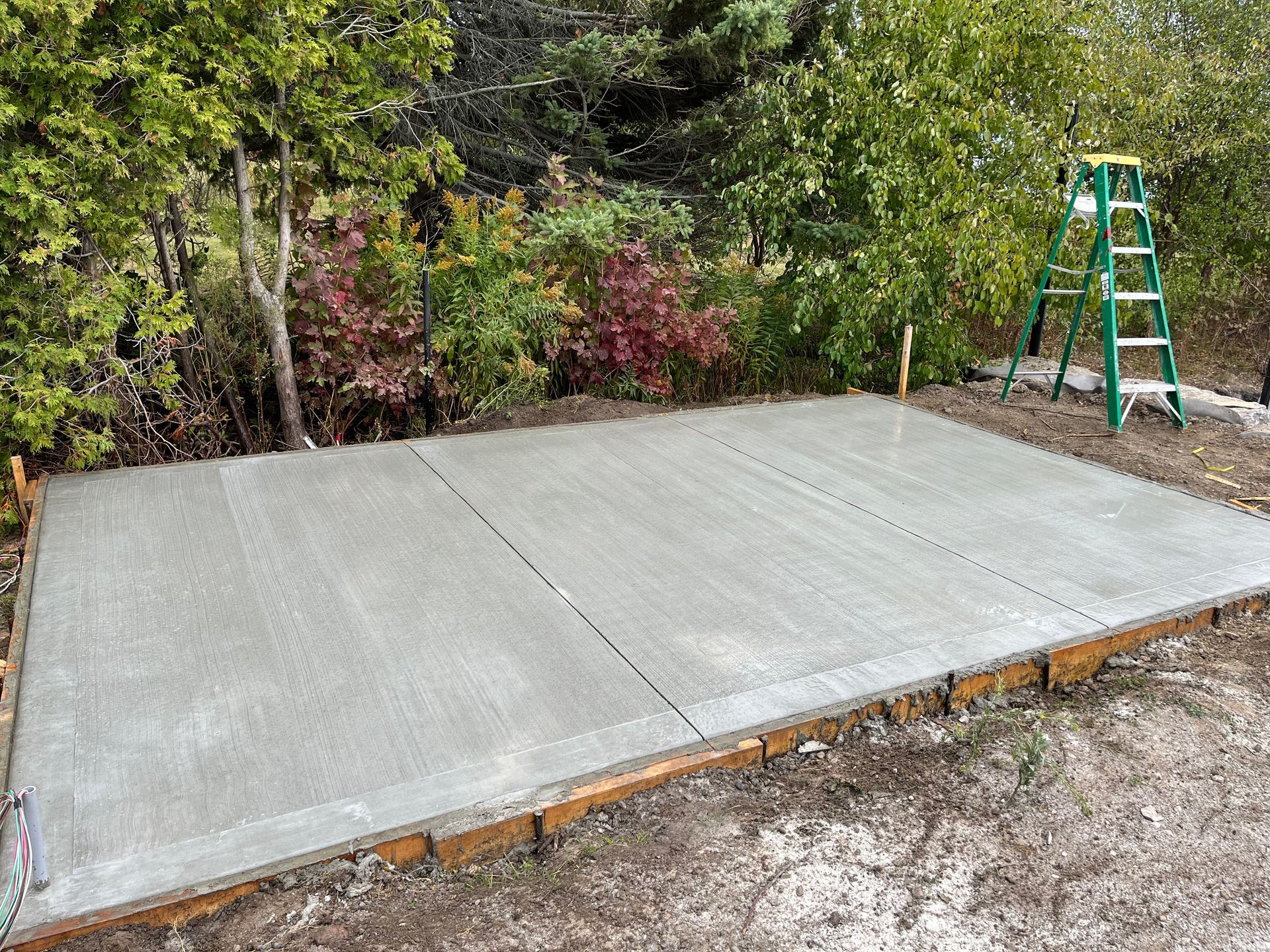 A concrete floor is being built in a backyard with a ladder.