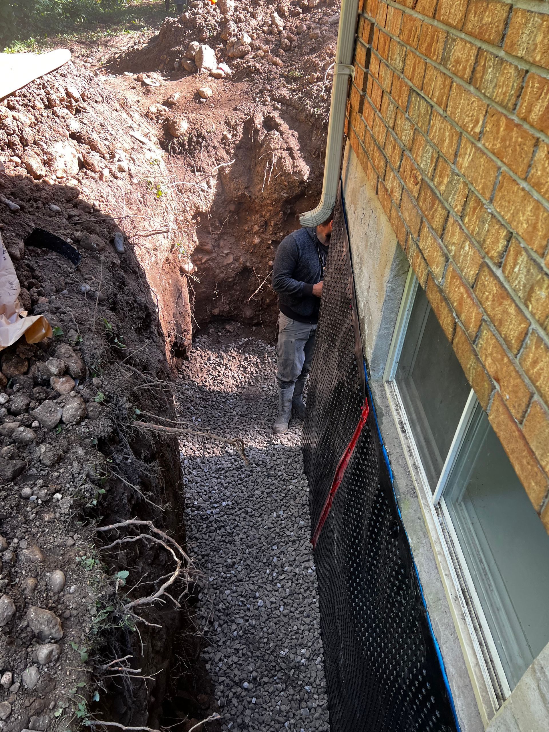 A man is digging a hole in front of a brick building.