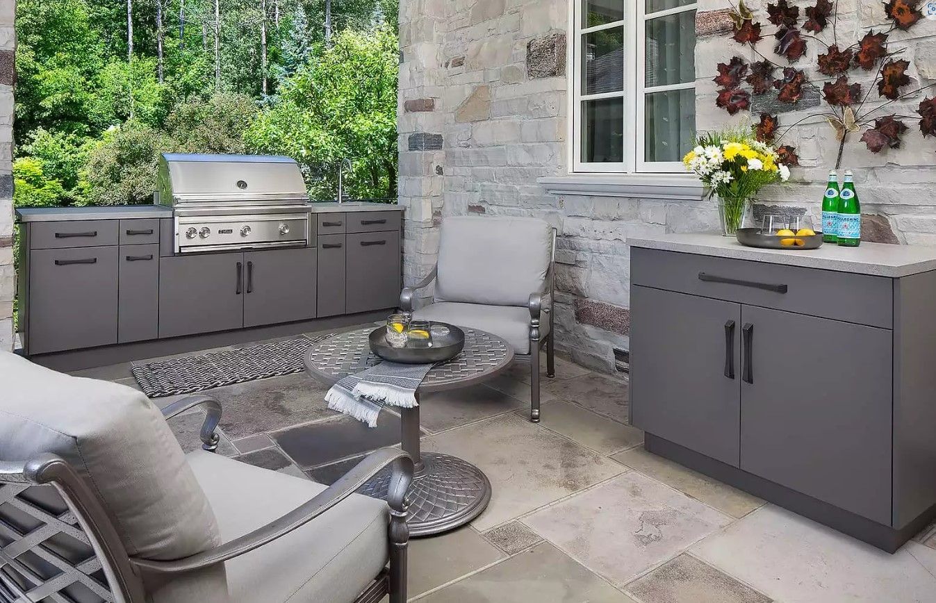 A patio with a grill , chairs , table and cabinets.