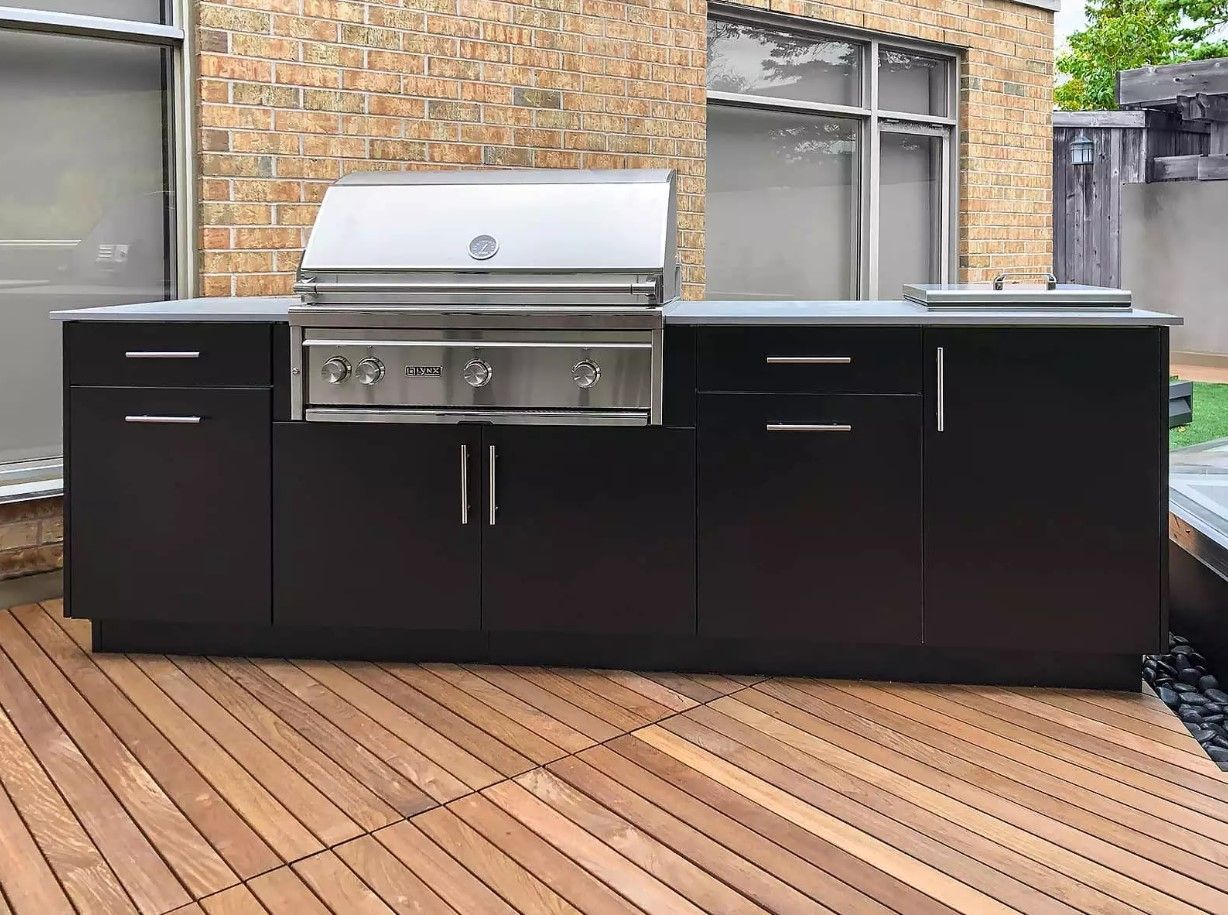 A large outdoor kitchen with black cabinets and a grill on a wooden deck.