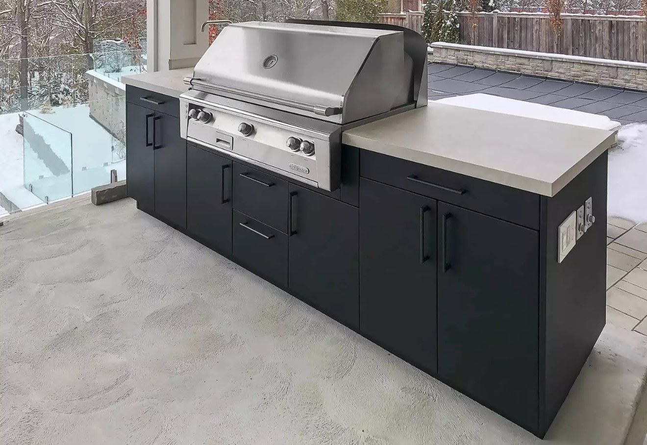 A large outdoor kitchen with black cabinets and a stainless steel grill.