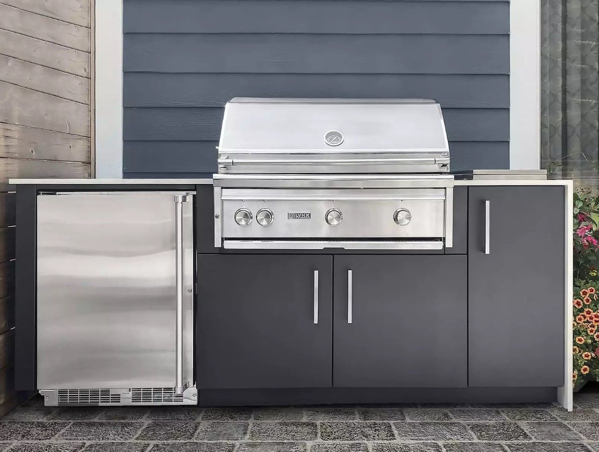 An outdoor kitchen with a grill and a refrigerator.