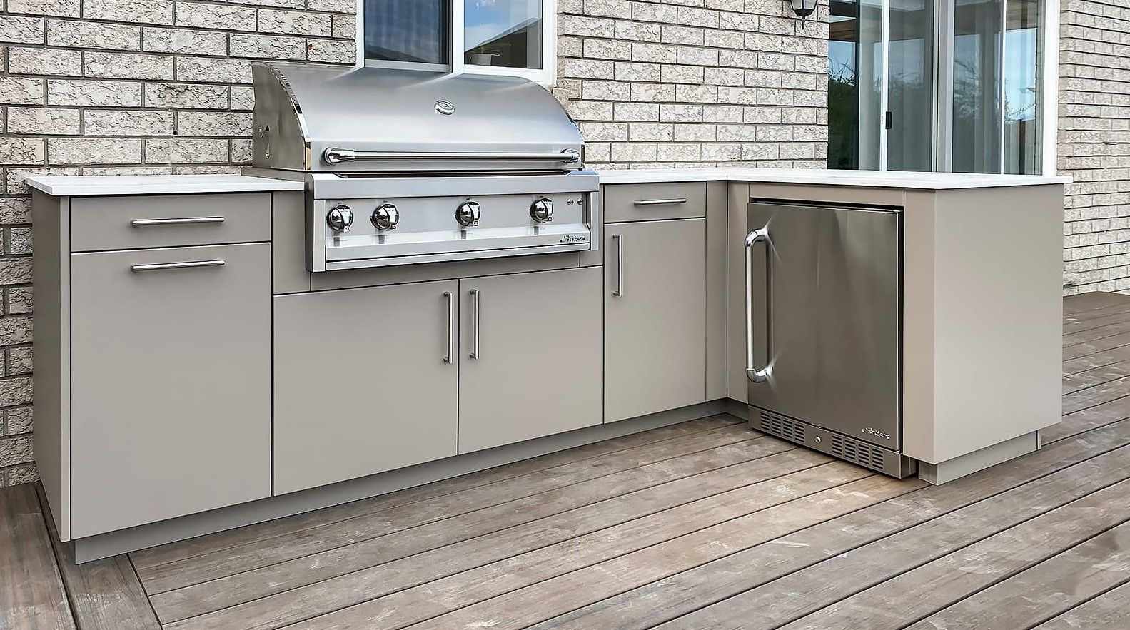 An outdoor kitchen with a grill and a refrigerator on a wooden deck.