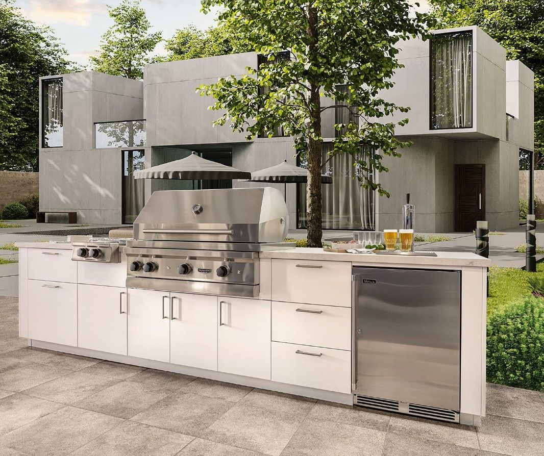 An outdoor kitchen with stainless steel appliances and white cabinets in front of a modern house.