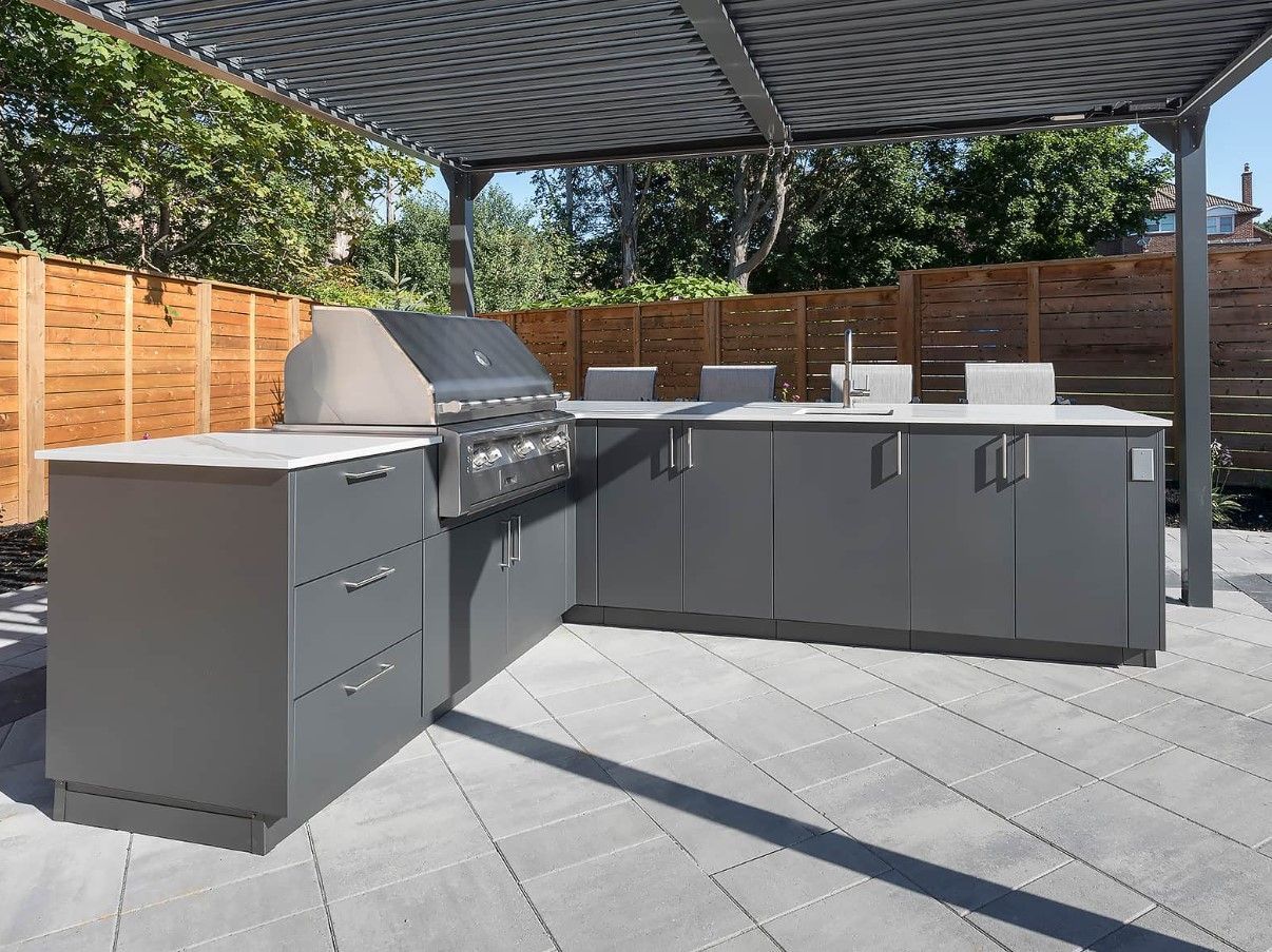 A large outdoor kitchen with a grill and cabinets under a canopy.