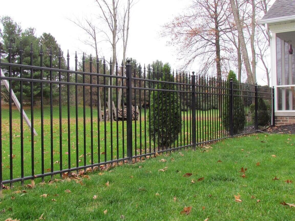 A black metal fence surrounds a lush green field in front of a house.