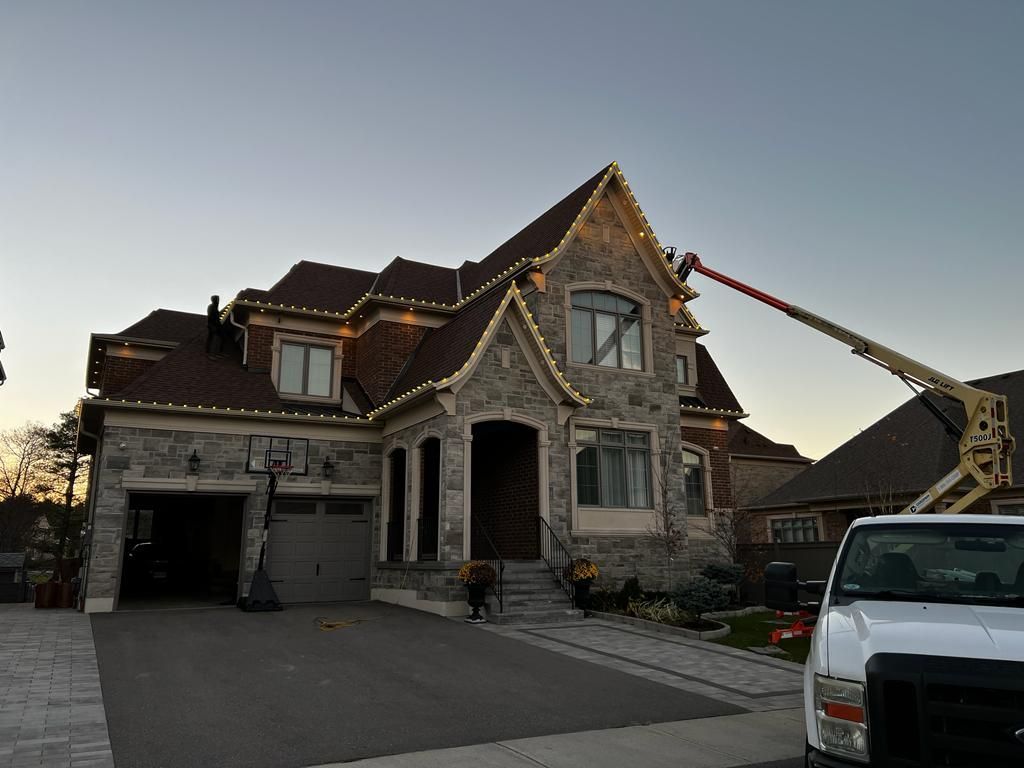 A white truck is parked in front of a large house with christmas lights on the roof.