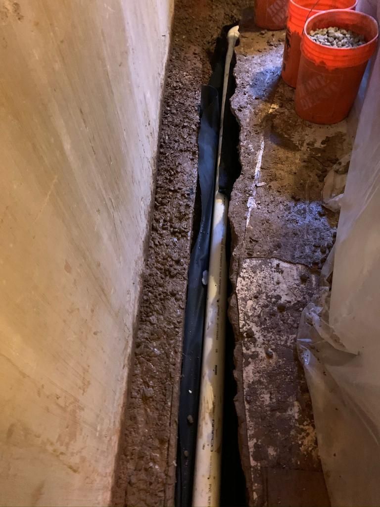 A pipe is being installed in a basement next to a wall.