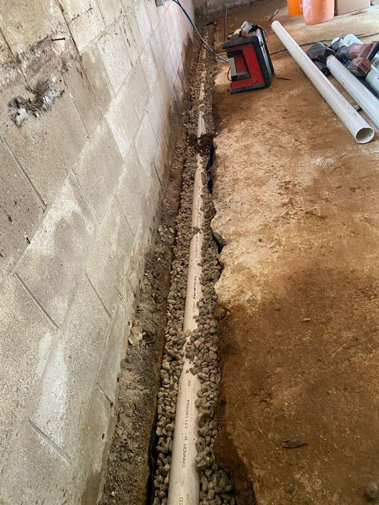 A drain pipe is being installed in a basement next to a brick wall.