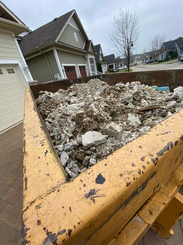 A yellow dumpster filled with rocks and dirt in front of a house.