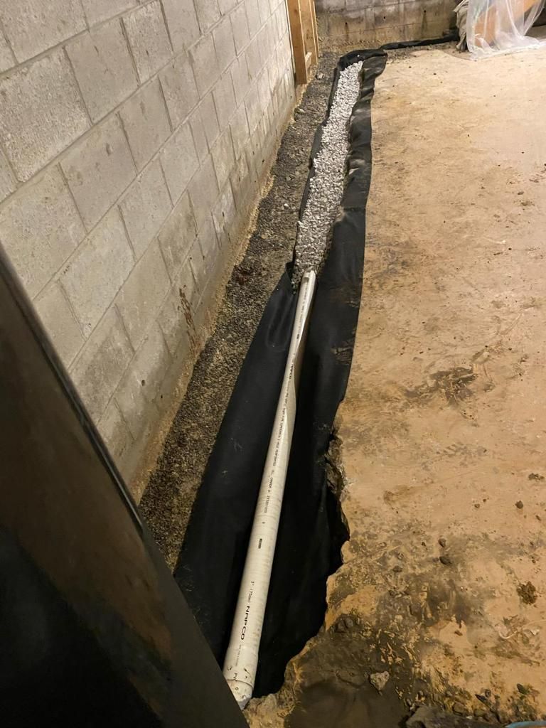 A drain pipe is being installed in a basement next to a brick wall.