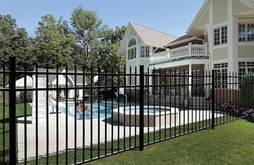 A large house with a swimming pool behind a metal fence.