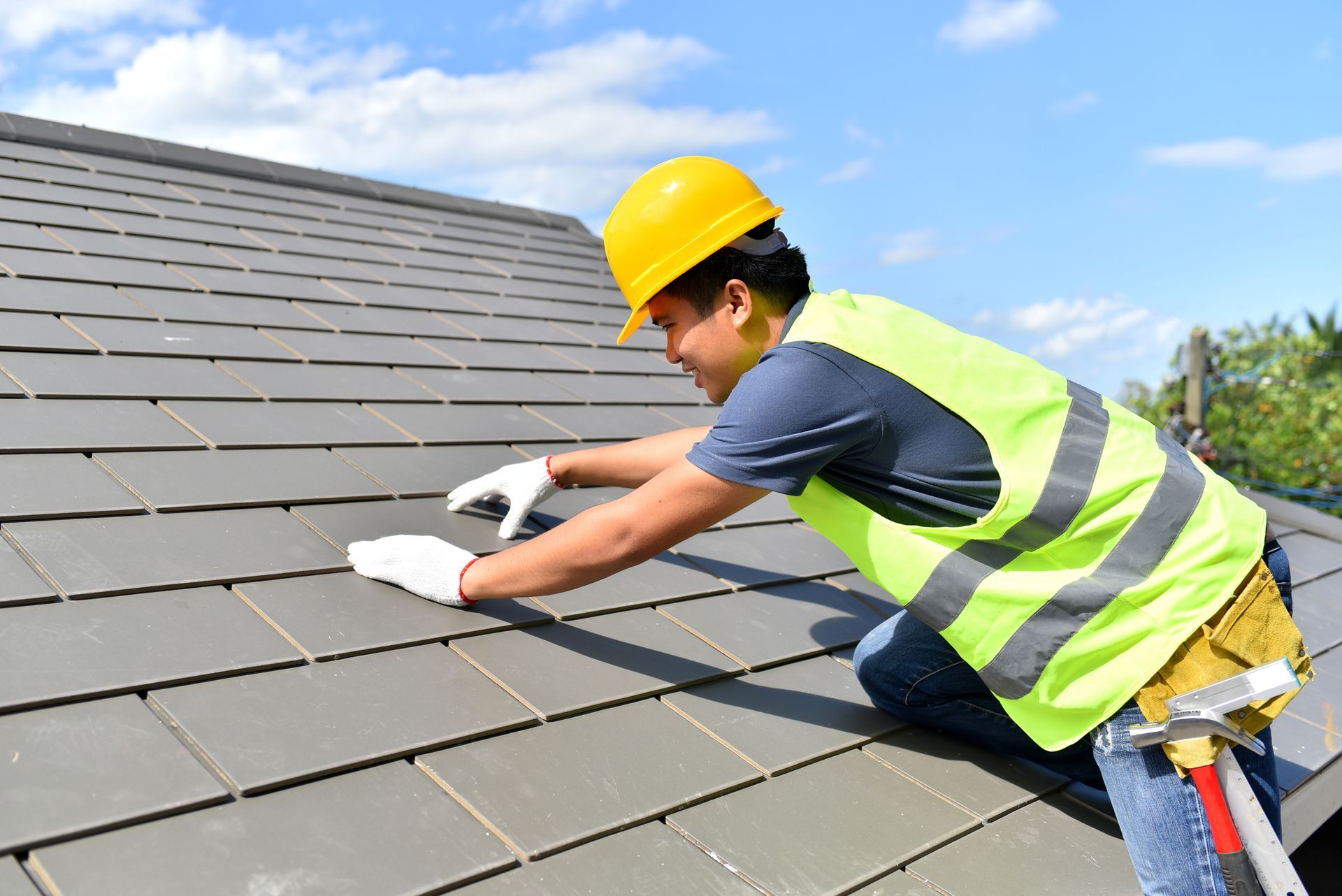 A man wearing a hard hat and safety vest is working on a roof.