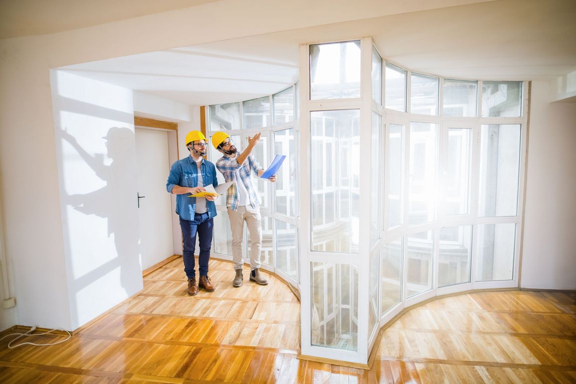 Two construction workers are standing in an empty room looking at a blueprint.