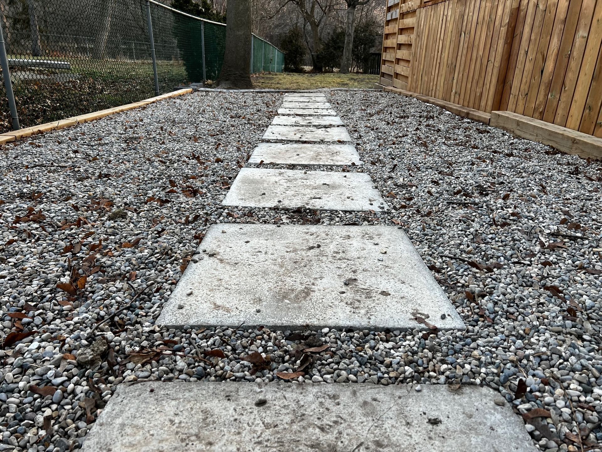 A stone walkway leading to a wooden fence in a gravel yard.