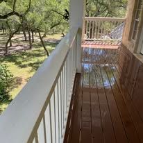 A wooden porch with a white railing and a view of a park.