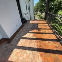 A balcony with a brick floor and a wrought iron railing.