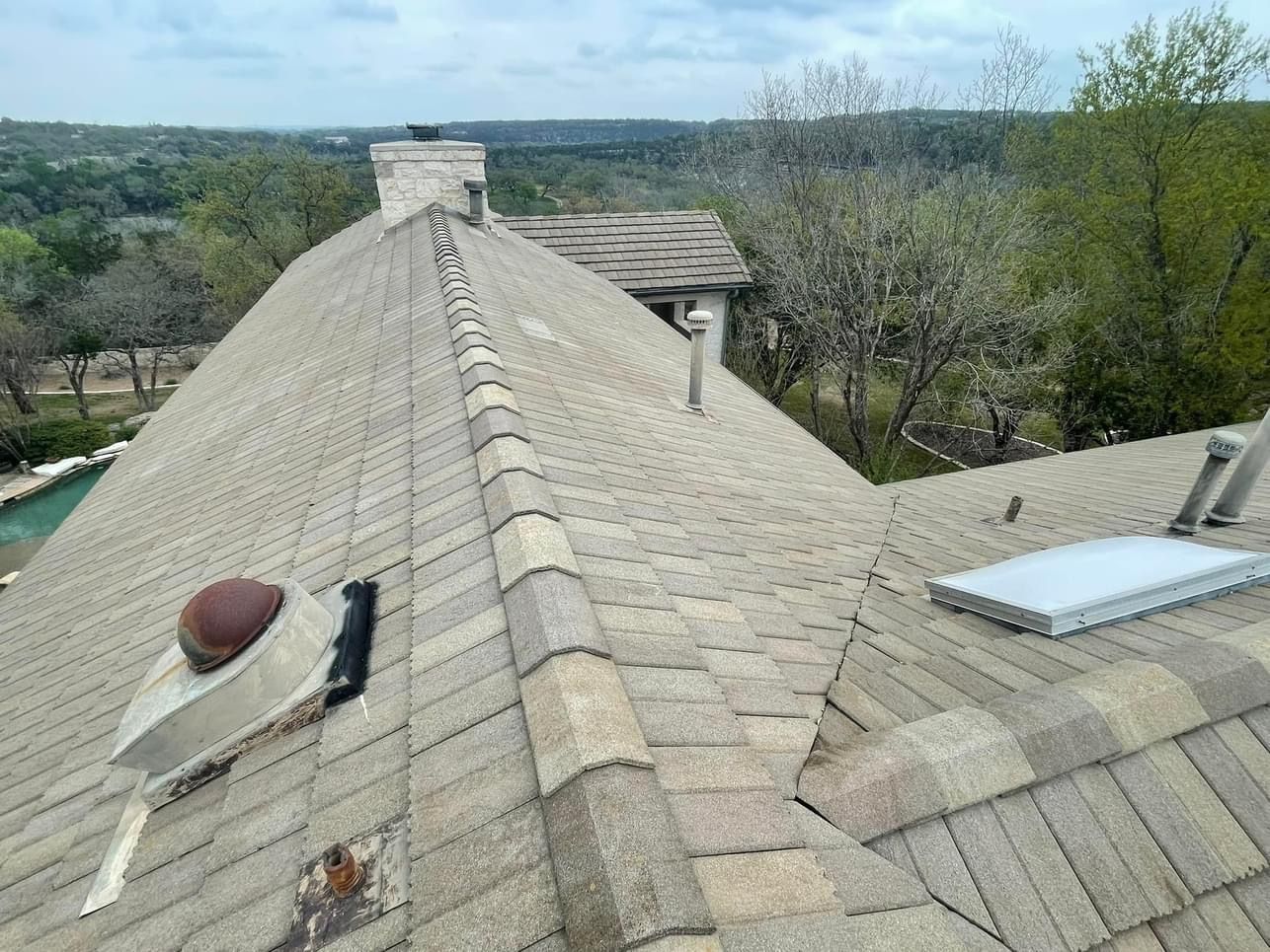 Asphalt shingle roof with vent pipes, chimney, and skylight. Overlooks trees and landscape.