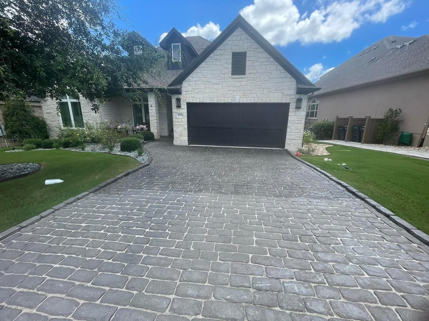 A brick driveway leading to a house with a black garage door