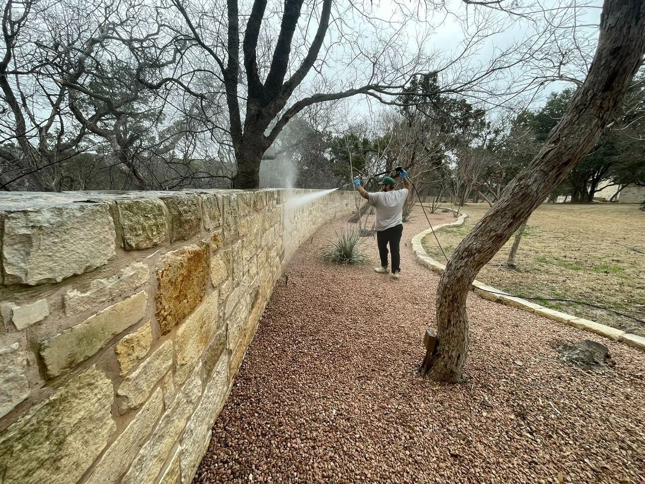 A man is cleaning a stone wall with a pressure washer.