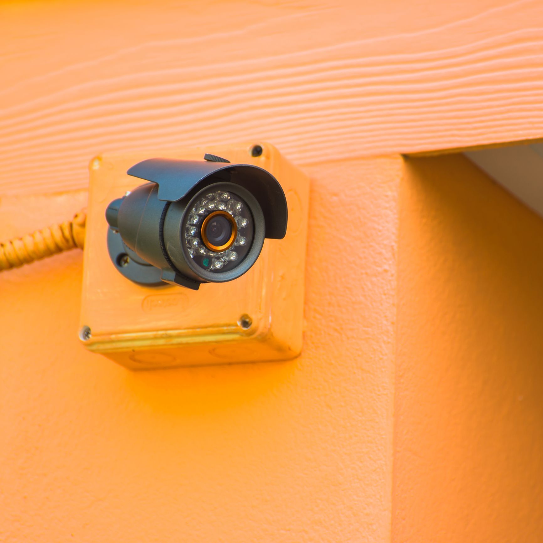 Black security camera installed on an orange wall.