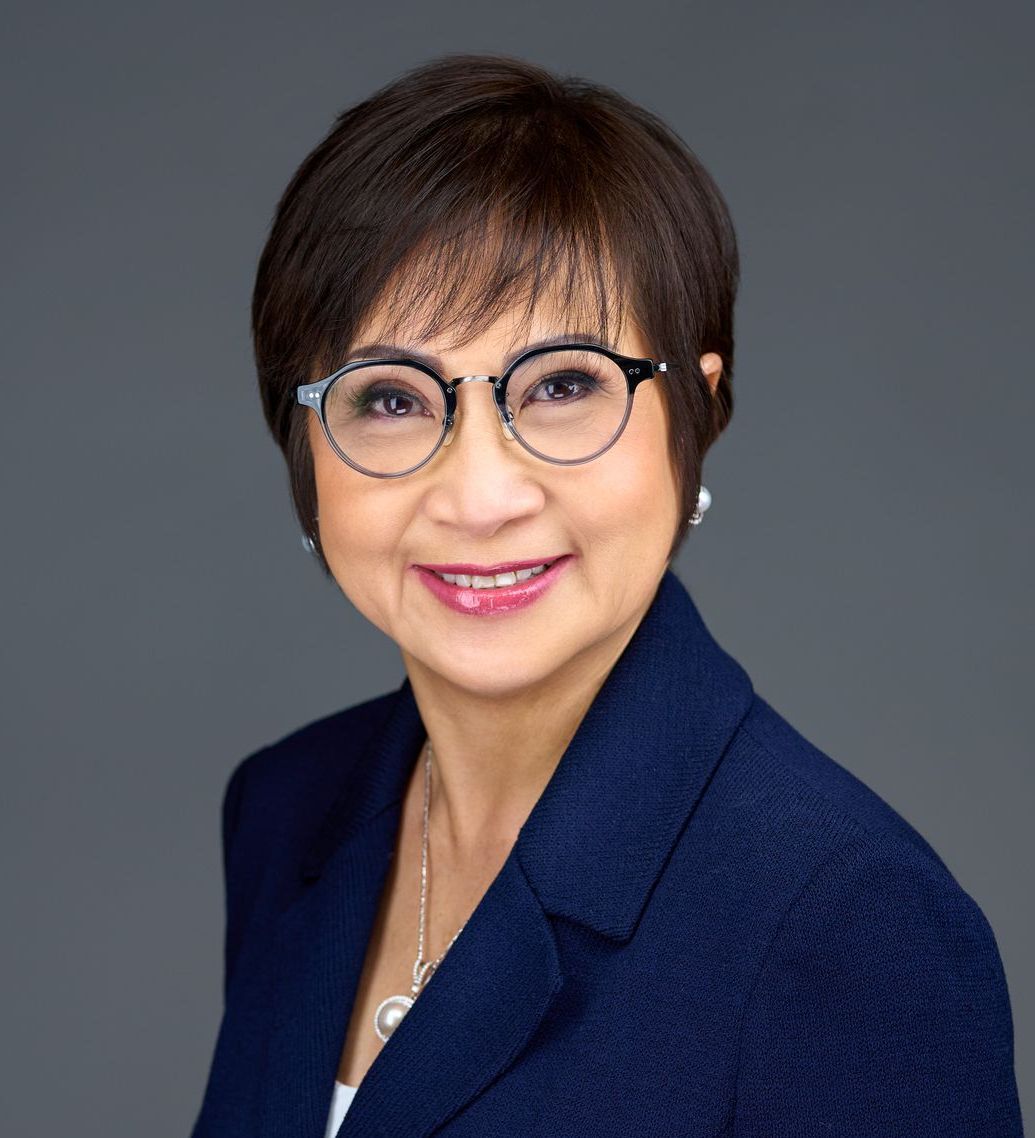 A woman wearing glasses and a blue jacket is smiling for the camera.
