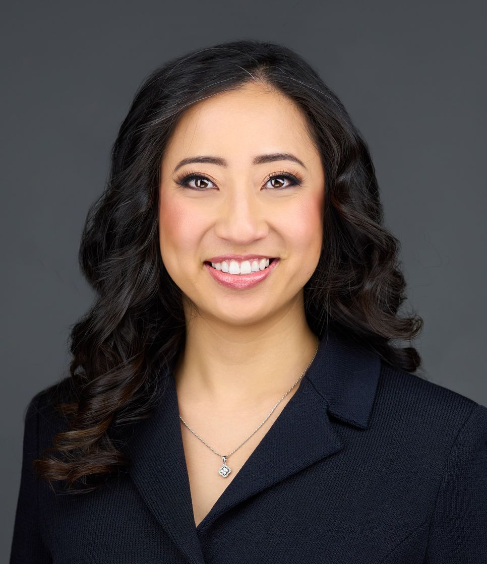 A woman wearing a black jacket and a necklace is smiling for the camera.