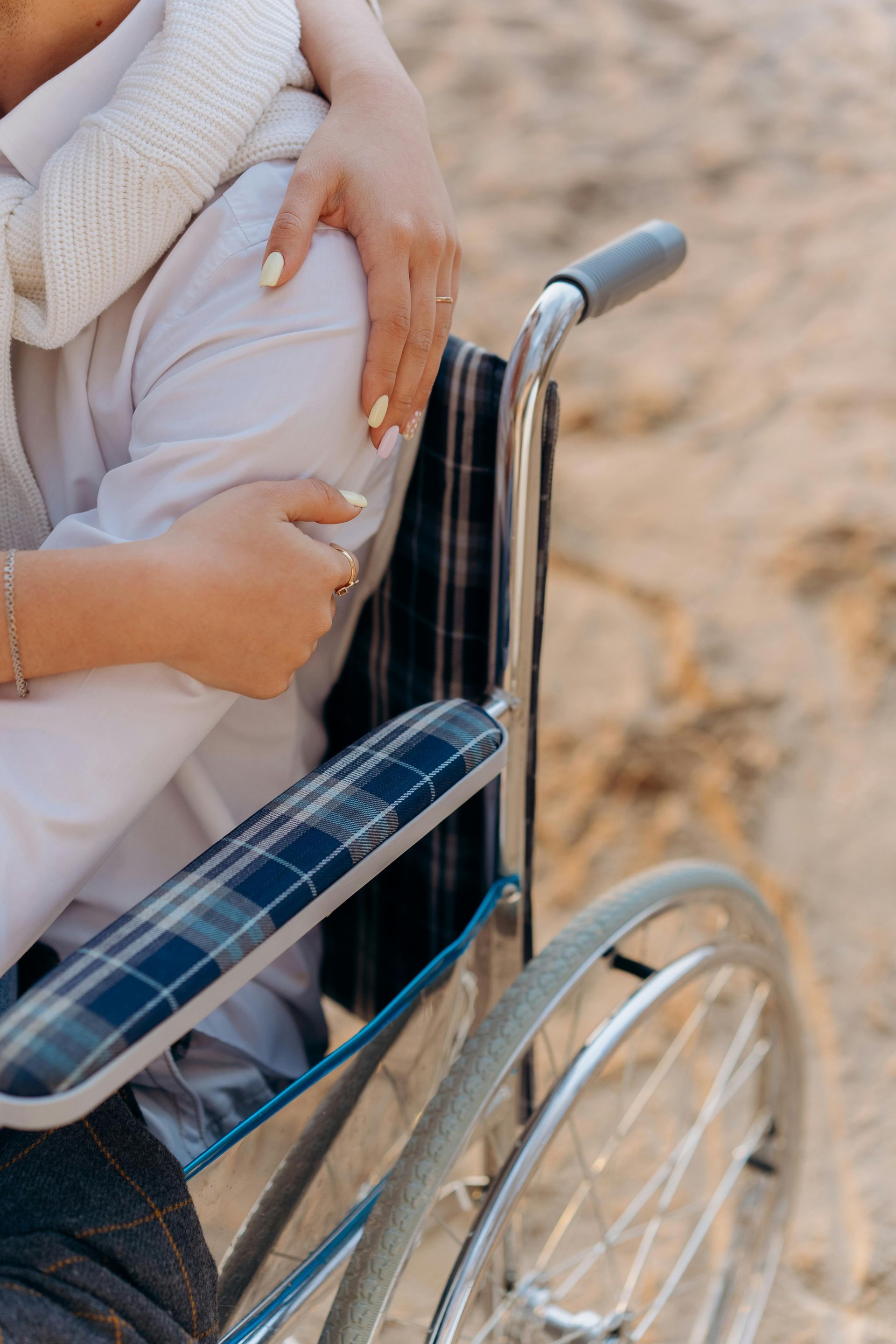 A woman is hugging a man in a wheelchair on the beach.