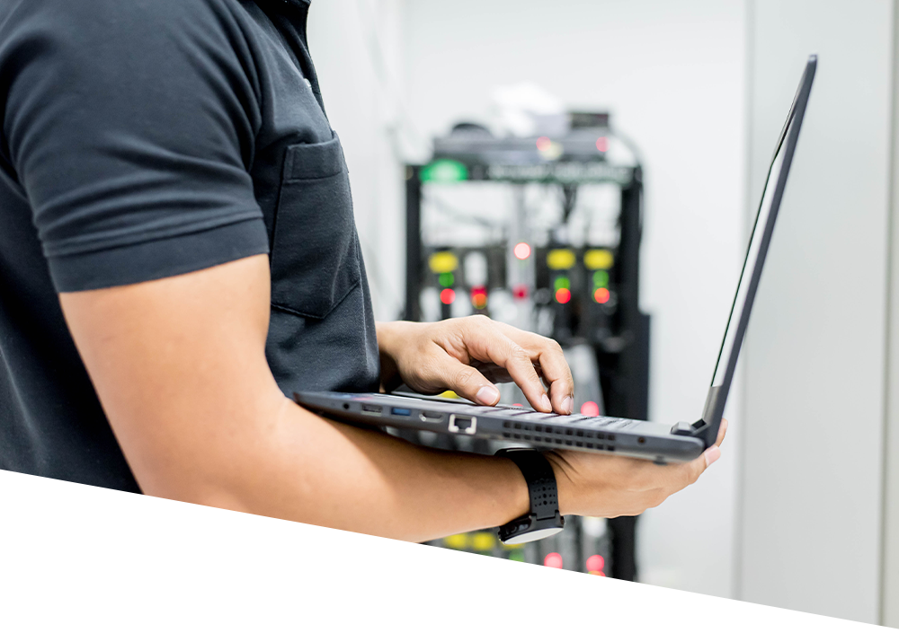 A man is using a laptop computer in a server room.