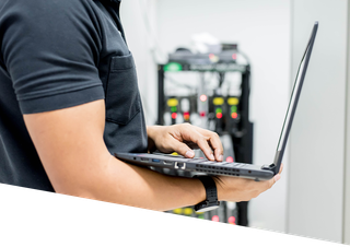 A man is using a laptop computer in a server room.
