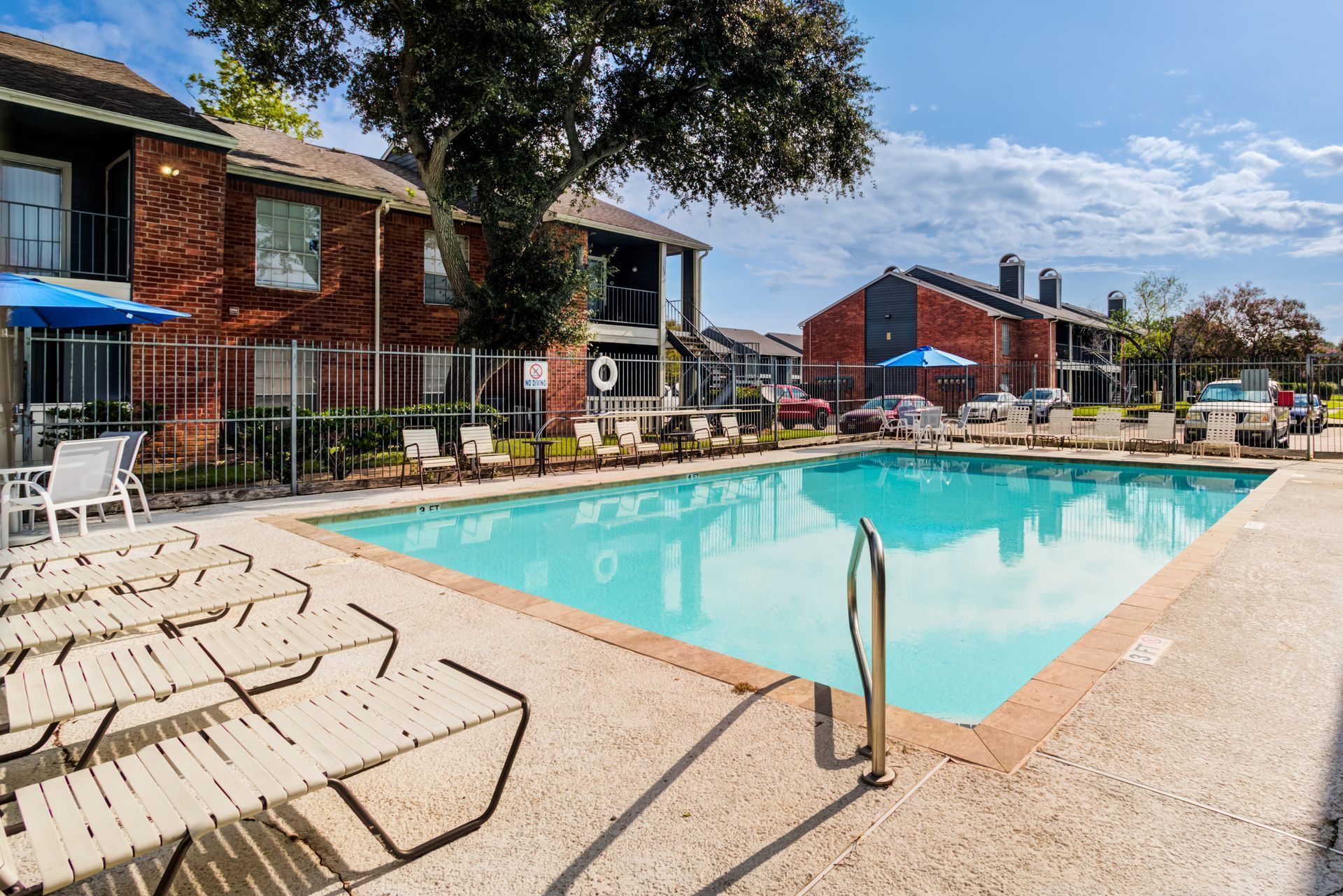 Swimming pool surrounded by lounge chairs, in front of an apartment complex on a sunny day.