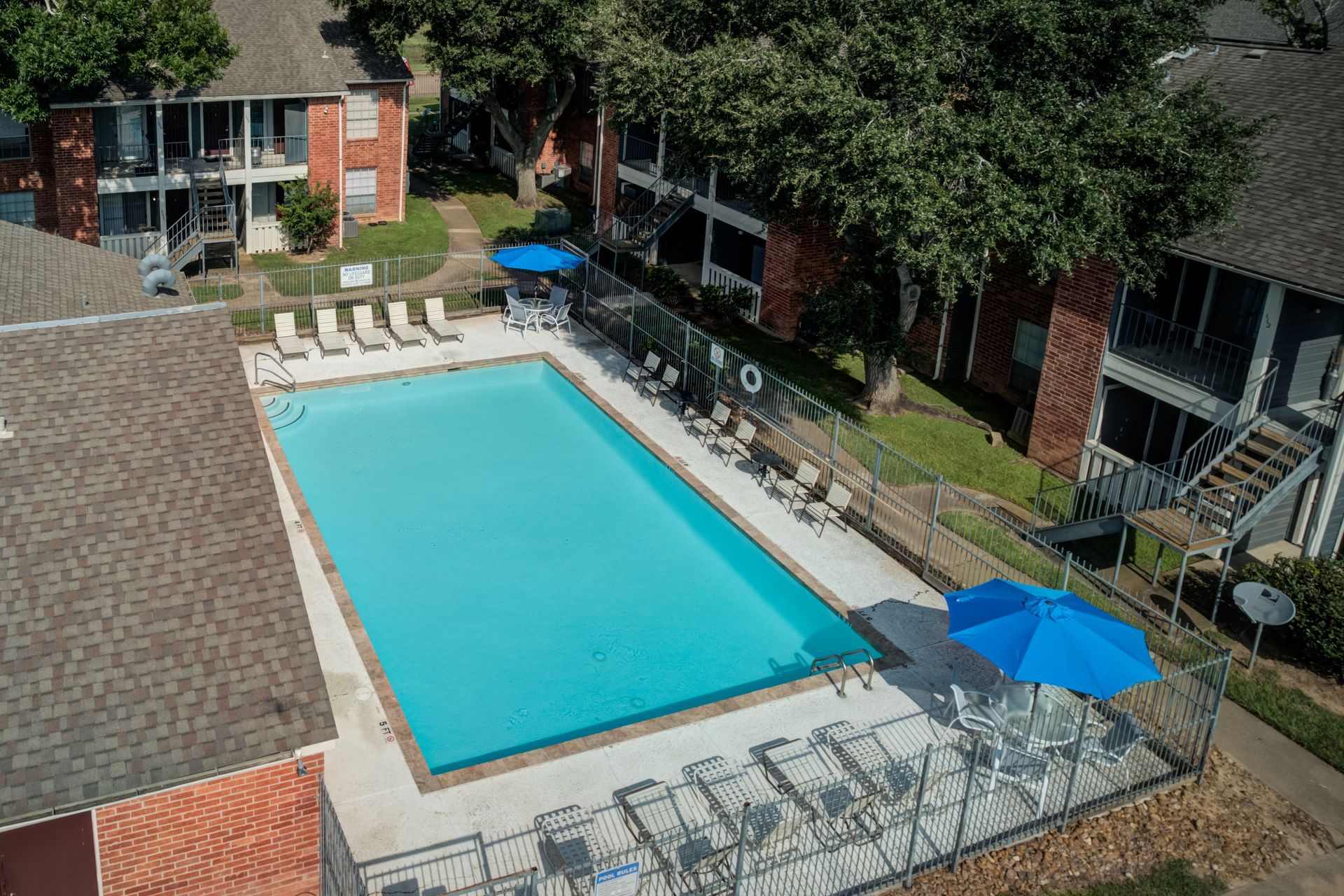 Swimming pool surrounded by apartment buildings, with blue umbrellas and lounge chairs.