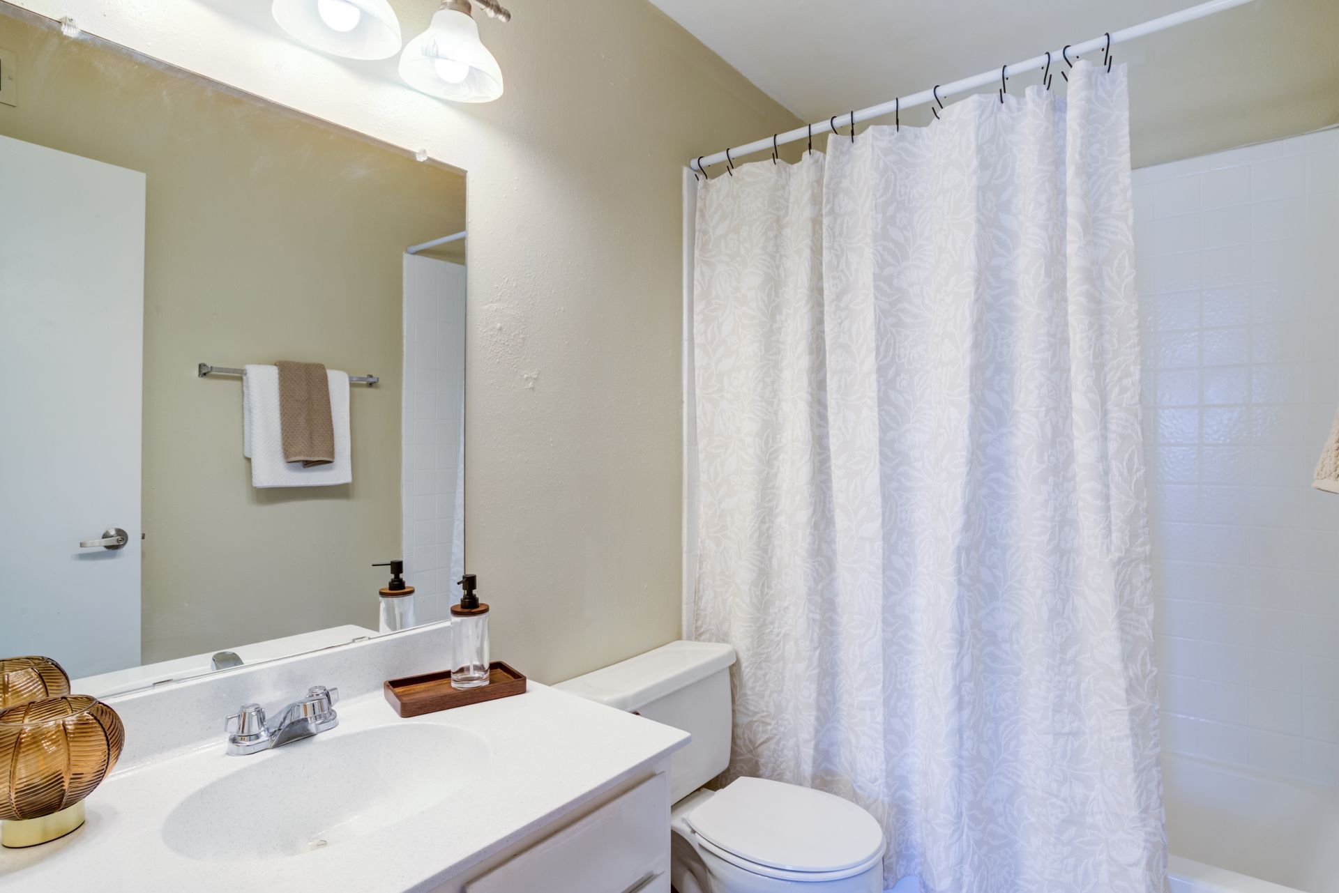 Bathroom with white sink, toilet, and shower curtain. Beige walls, towel, and light fixture.