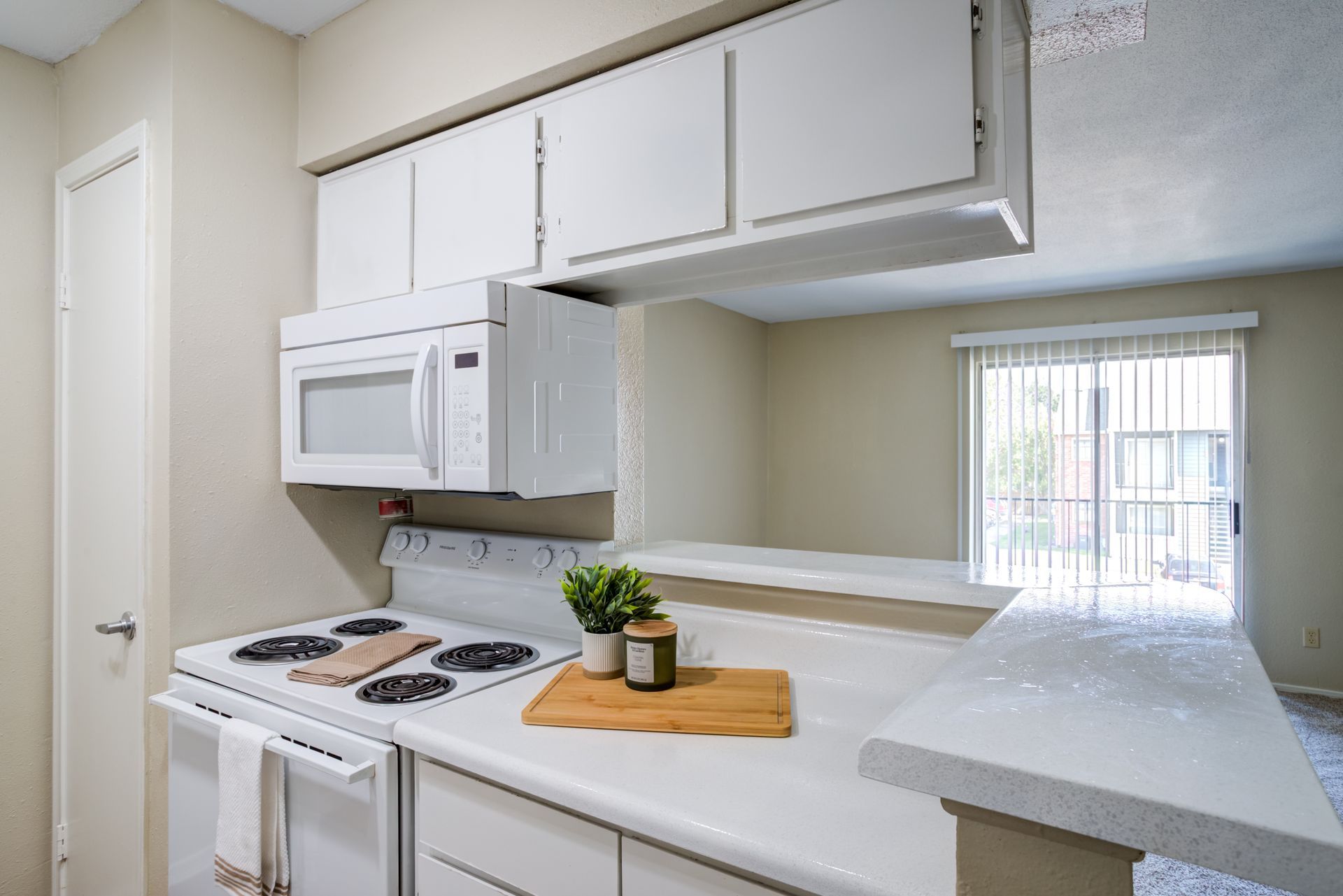 Kitchen with white cabinets, microwave, stove, and countertop. Sliding door visible.