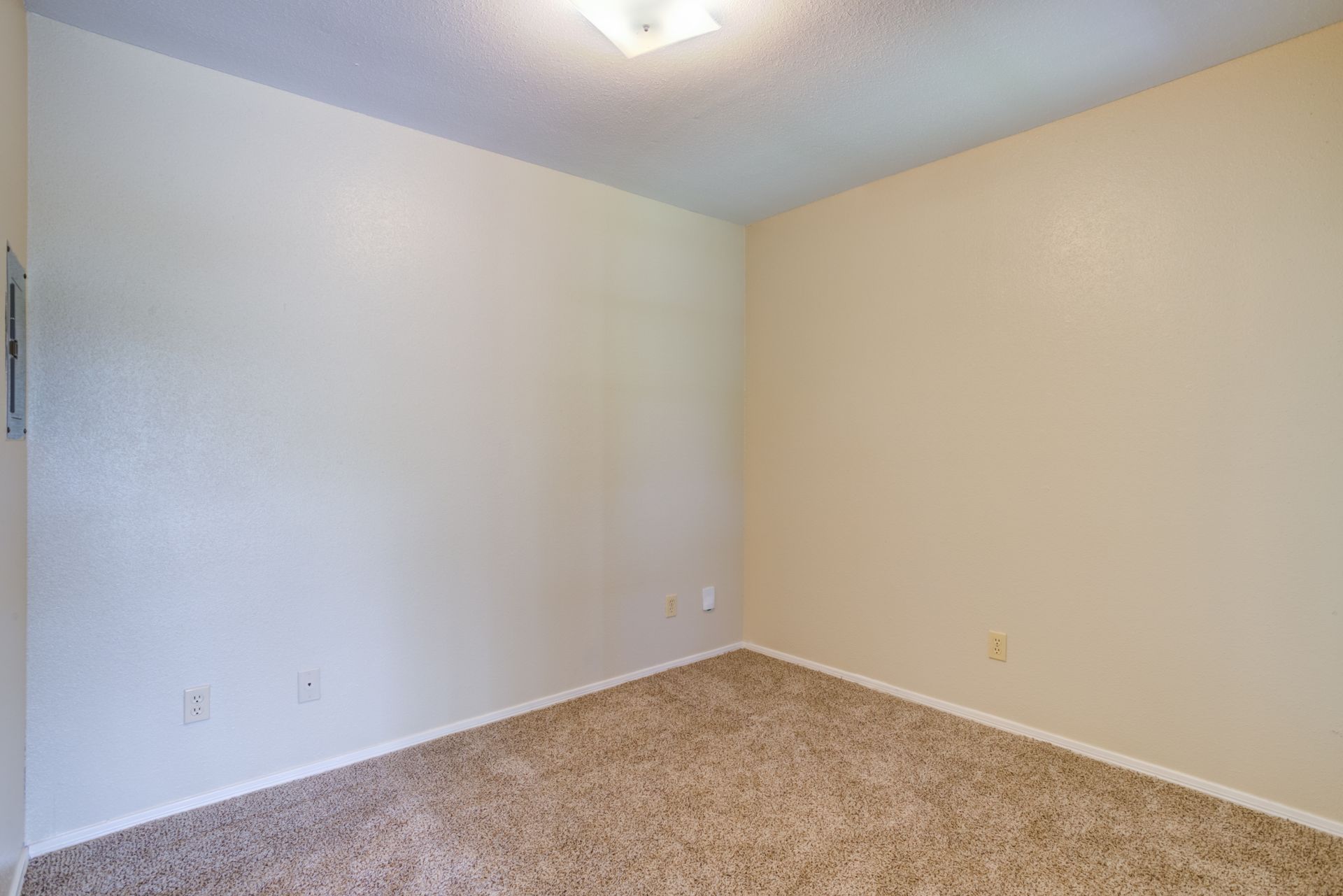 Empty room with tan walls and carpet; white trim and ceiling with light fixture.
