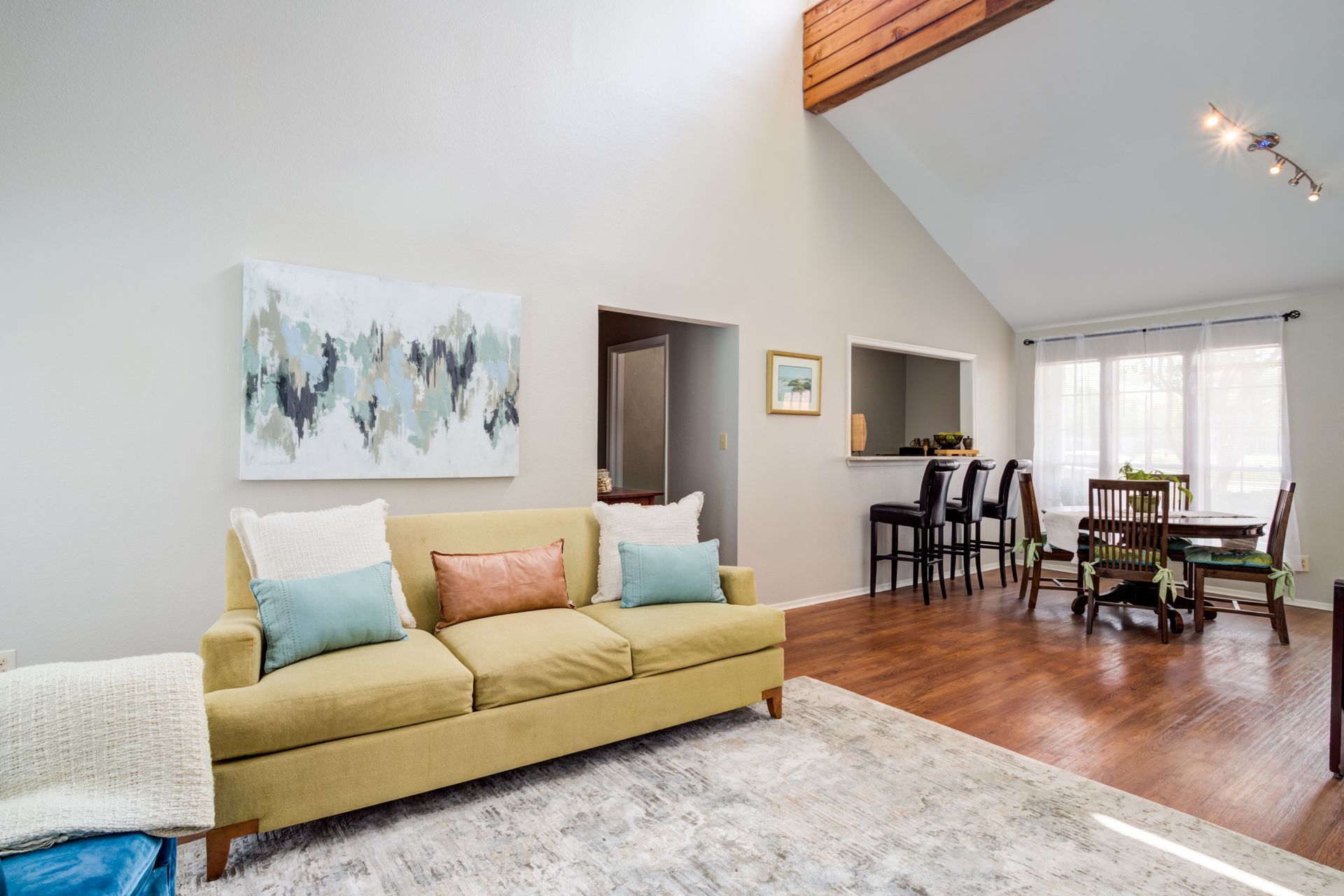 Living room with yellow couch, abstract art, dining area, and high ceilings.