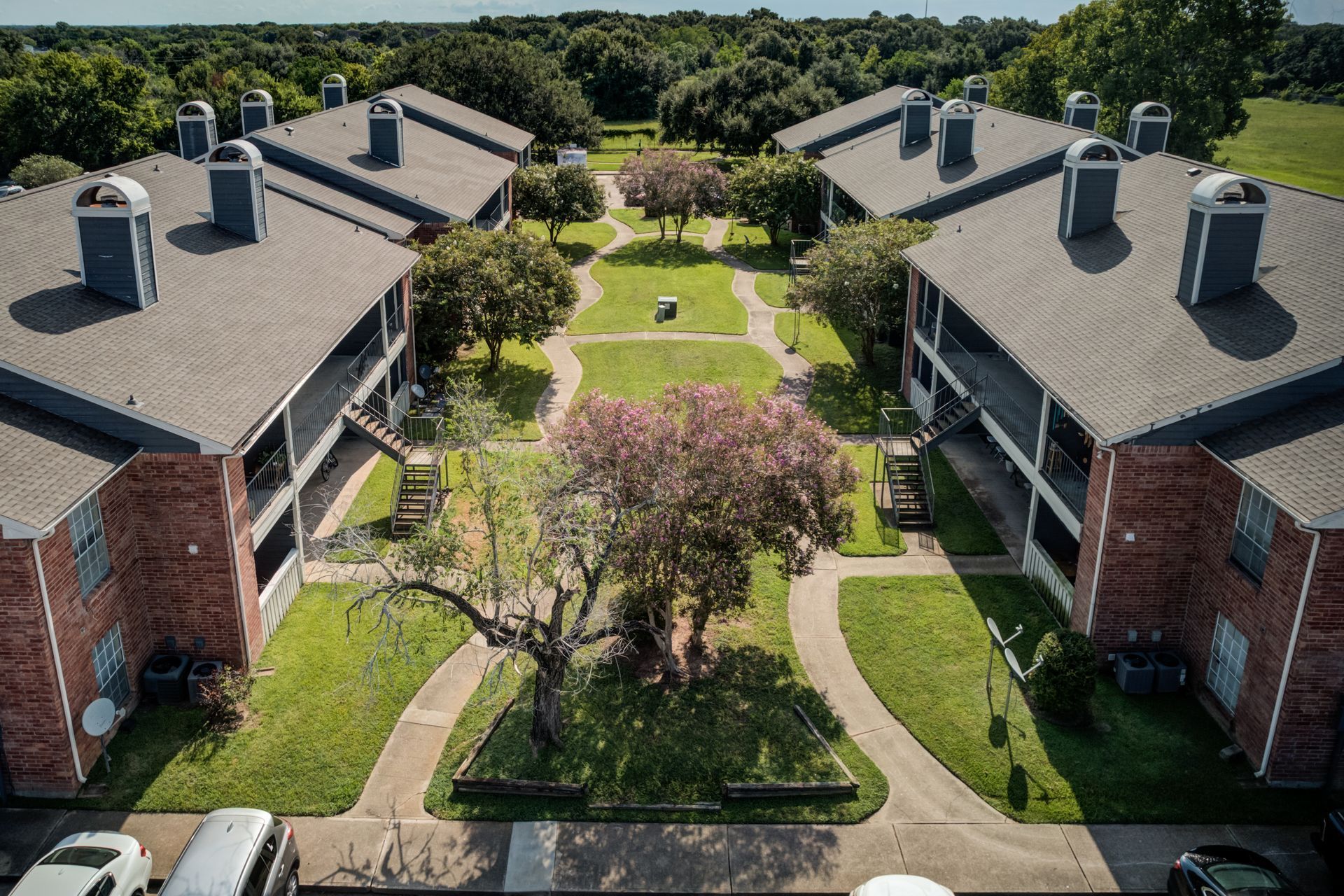 Aerial view of brick apartment buildings with gray roofs, green lawns, and trees.