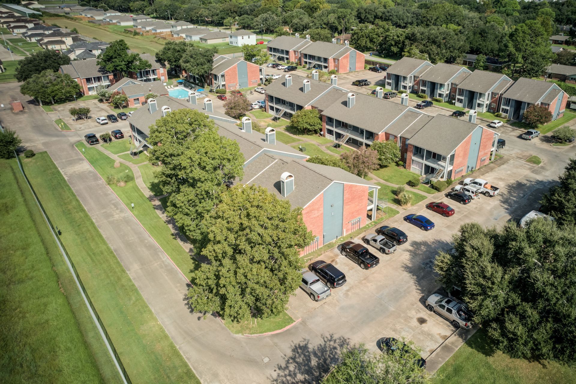 Aerial view of an apartment complex with multiple two-story buildings, parking, and a green lawn.